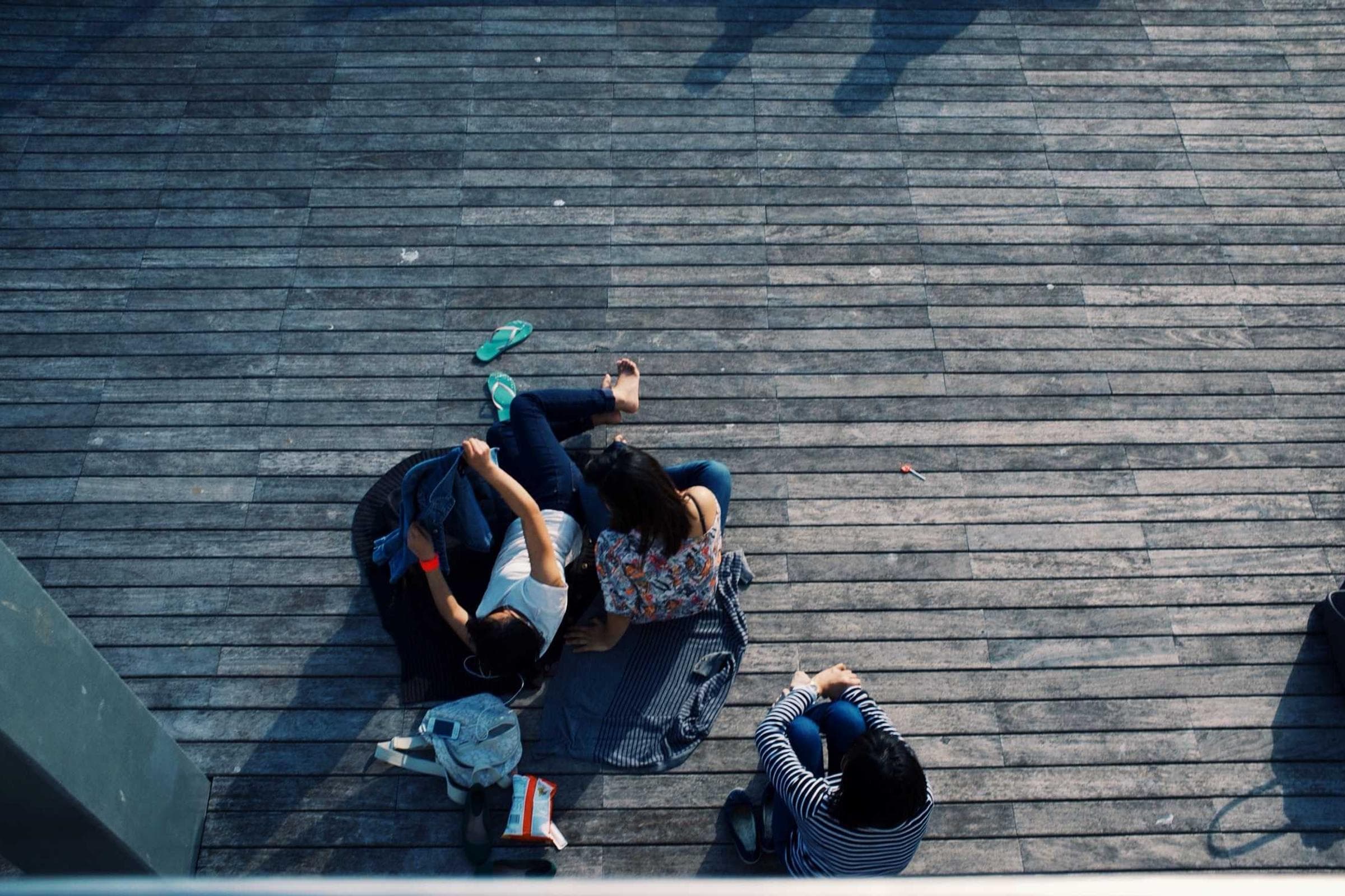 A small group of people lying and sitting together on a wooden boardwalk, seen from directly above